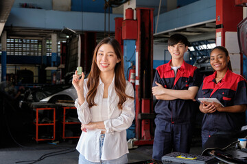 Young Asian female customer shows car key with automotive mechanic workers, happy smile in quality...