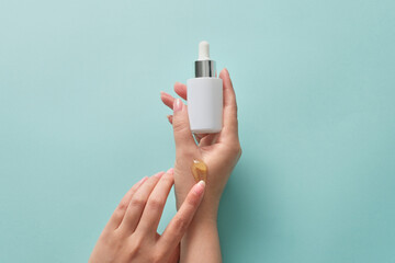 Beautiful female hand is holding a serum bottle with dropper and applying yellow essence into her...