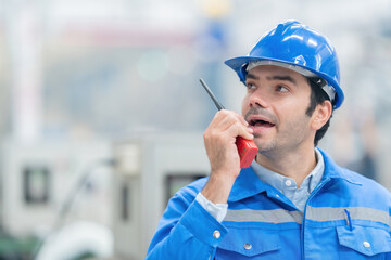 Close-up photo of American male engineer Working diligently and determinedly communicating by radio with employees Wearing uniforms, helmets, Machines working in a large plastic and steel industry
