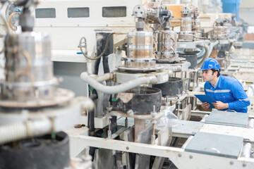 American male engineer Stand amongst the machines working around you. Holding a listnote checking the system's stability Wearing a uniform, helmet, in a large plastic and steel industry