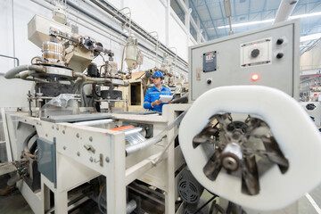 American male engineer Standing to control the work system in the middle of the machine that produces plastic materials. in large industrial plants Wear helmets, uniforms and listnotes.