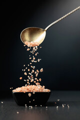 Pink salt is poured into a small black bowl.