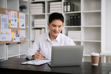 Young Asian business man using laptop and tablet while sitting at her working place. Concentrated...