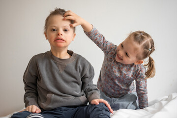 Boy plays with his younger sister on the bed in home bedroom. Down syndrome and ASD
