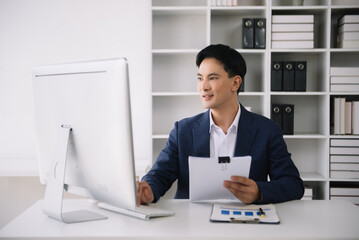 Fototapeta na wymiar Confident Asian man with a smile standing holding notepad and tablet at the modern office.