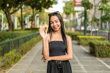 A pretty young lady standing in the park wearing a black strapless tank top and sunglasses, smiling...