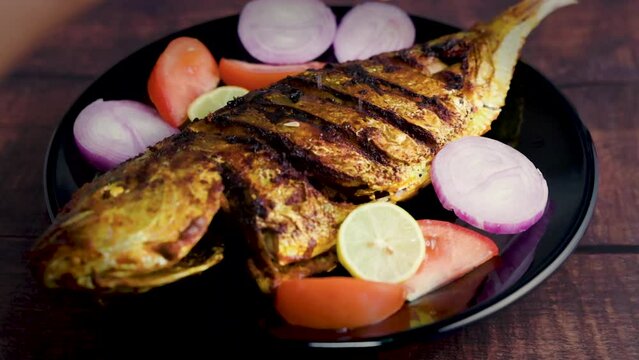 Delicious fried fish or fish fry on a black plate with onion, tomato, and lemon. Spicy Indian Kerala style fish fry on a wooden table. Lemon squeezed over grilled fish.