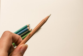 A hand holding a blending pencil for colored pencils with several colored pencils in the background on a white surface