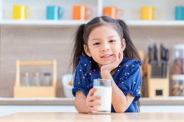 Cute little girl with glass of milk at table in kitchen, Happy child girl drinks milk