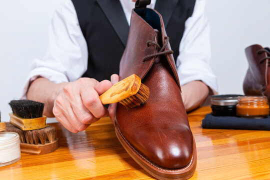 Closeup of Male Shoes Cleaner with Cleaning Brushes For Tan Derby Leather Boots While Working in Workshop With Rub Cloth