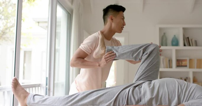 Diverse male physiotherapist advising and senior male patient stretching, in slow motion
