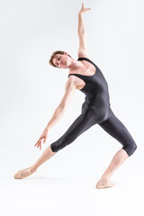 Naklejka premium Modern Ballet Dancer Young Caucasian Athletic Man in Black Suit Posing Stretching in Studio On White With Lifted Hands.