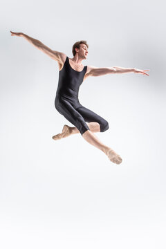 Ballet Dancer Young Caucasian Athletic Man in Black Suit Dancing in Studio Over White Background With Lifted Hands.