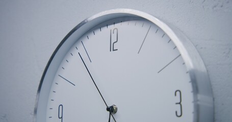 Static shot of white watch with metal frame hanging on the wall and showing time. Walking wall clock in office with modern design. Strict clock with fast running time pointer. Close up.