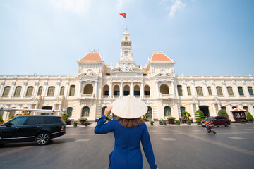 Asian woman is wearing Ao Dai traditional Vietnamese dress and traveling at Hochiminh people's committee hall landmark of Saigon, Vietnam.