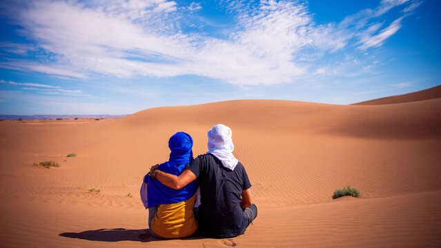 Couple sitting in the desert looking at panoramic view of sand dunes