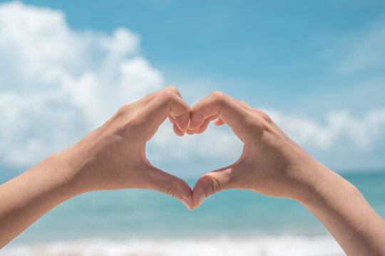 Hand do heart shape mean love on nature summer beach and blue sky background.
