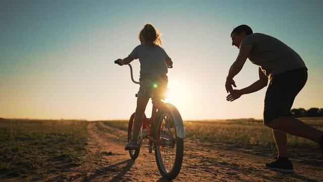 Happy family. Father teaches daughter to ride bike in park. father helps his daughter in her studies. happy child dreams of traveling by bike. child is learning to ride bike.