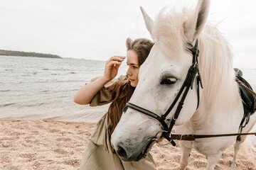 A white horse and a woman in a dress stand on a beach, with the sky and sea creating a picturesque...