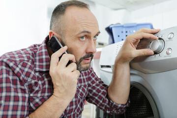 man talking onphone while putting laundry in washing machine