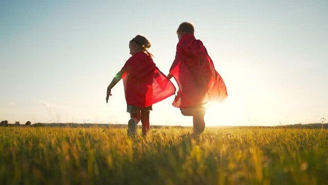 Team of superheroes runs across field in suit. group of children with dog play in superhero cape at sunset. Children with dog run across field of park. Children's dream of freedom.