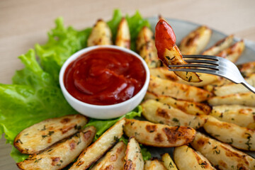 Baked potato wedges with herbs, salt, spices and tomato sauce. Baked spiced potatoes look delicious. Snack for beer. Close-up.