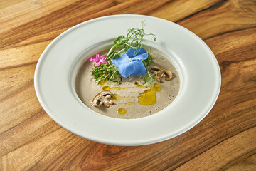 Cream of mushroom soup with decorative flowers in a white plate. Vegetarian food