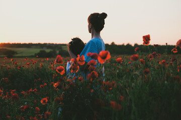 Mom, hugging her daughter, stand in a field with flowering poppies