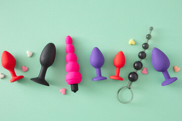 Concept of anal toys for sexual satisfaction. Top view arrangement of anal plugs and balls, colorful hearts on turquoise background - obrazy, fototapety, plakaty