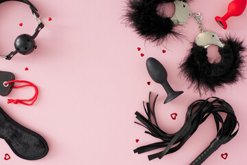 Array of pleasure toys for BDSM adventures. Top view photo of feather handcuffs, leather whip, ball gag, anal plugs, red hearts on pastel pink background with empty space for text or advert - obrazy, fototapety, plakaty