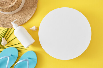 The idea of summer skincare while on vacation. Top view composition of sunscreen pump bottle, flip flops, straw hat, palm leaf, seashells on yellow background with blank circle for advert or text