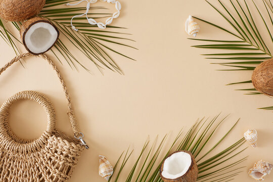 The idea of a summer seashore getaway. Top view composition of straw handbag, ripe coconuts, tropical leaves, shell bracelet, seashell on pastel beige background with space for promo or message