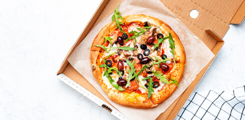 Hot Pizza in box with salami sausage, mozzarella cheese, mushrooms, black olives, spicy tomato sauce and arugula, white table background, top view banner
