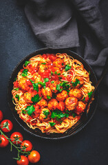 Prepared spaghetti pasta with fried pork meatballs in tomato sauce with parsley in frying pan, black table background, top view