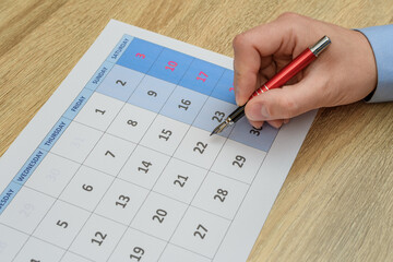Kartka z kalendarza na biurku, mężczyzna zaznacza termin dlugopisem