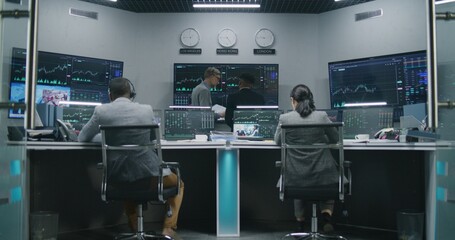 Multi ethnic team of traders work on multi-monitor computers with displayed real-time stocks. Colleagues analyze exchange market charts on big screens. Cryptocurrency trading and investment. Zoom out.