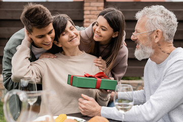 Positive children hugging middle aged mother near father while spending time during parents day celebration and family barbeque party at backyard in june, celebrating parenthood day concept