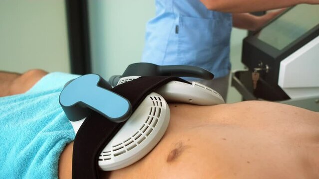 Beautician therapist applying burn fat and build muscles treatment in beauty salon to young man.