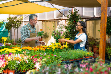 Happy female customer buying orange flowers from a gardener in a nursery inside the greenhouse in...
