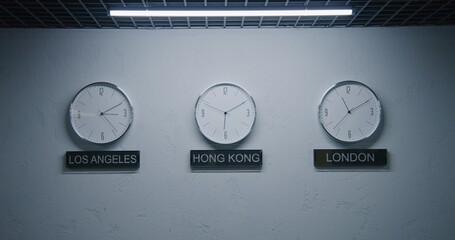 Static shot of white wall clocks with running time pointers illuminated by lamp in office with modern design. Names of big cities written under wall clocks. Watches showing time of different cities.