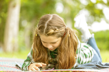 beautiful eight-year-old girl laying in the meadow doing homework, studying hard in the garden.