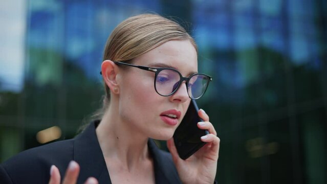 Determined assertive young businesswoman is engaged in a heated conversation on mobile phone outdoors. Unsatisfied female customer expressing dissatisfaction and frustration, using strong language.
