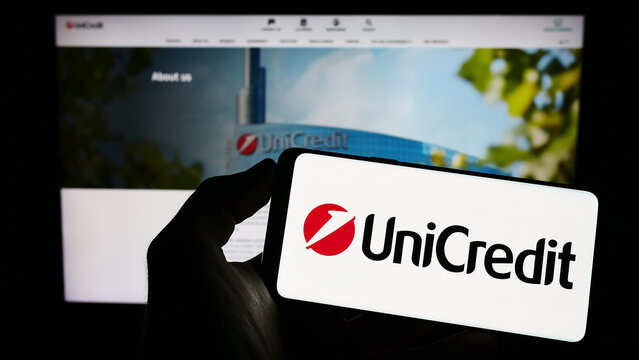 Stuttgart, Germany - 06-17-2023: Person holding mobile phone with logo of Italian financial company UniCredit S.p.A. on screen in front of web page. Focus on phone display.