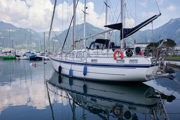 A beautiful white sailing ship is elegantly moored in the placid waters of a picturesque Italian lake port.