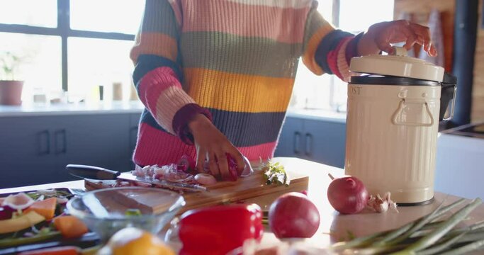 Mid section of african american woman composting vegetable waste in sunny kitchen, in slow motion