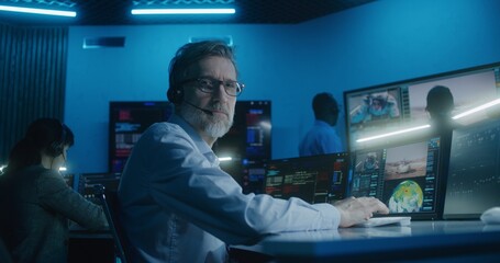 Flight control employee in headset sits in front of computers, monitors space mission in mission...