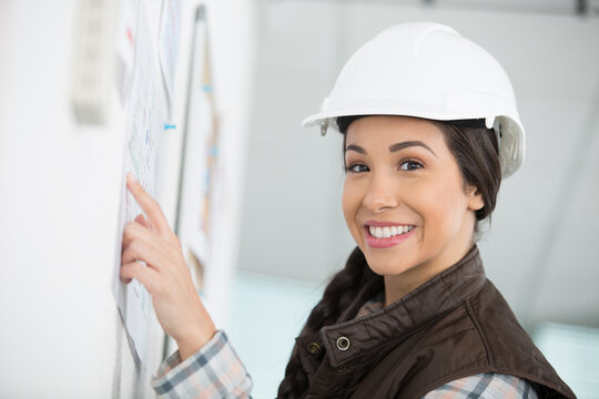 female worker wearing a hardhat pointing at noticeboard