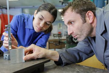 man and young woman worker checking measurements of metal workpiece
