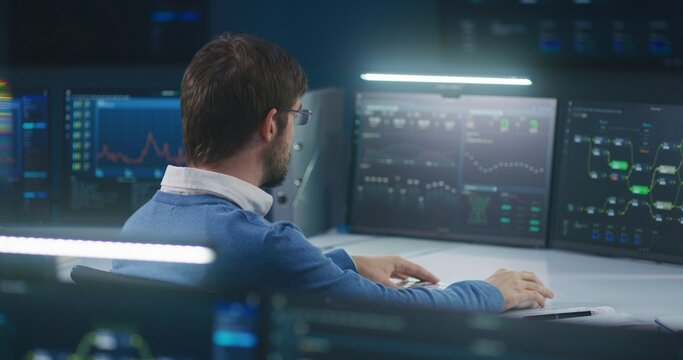 Professional software engineer sits in front of computer with big data server and blockchain network, works in modern monitoring control room with real-time analysis charts. Concept of cyber security.