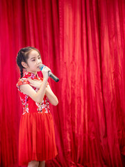 The Asian kid girl sing a song on stage at her school activity day, dress in Qipao style, red curtain background
